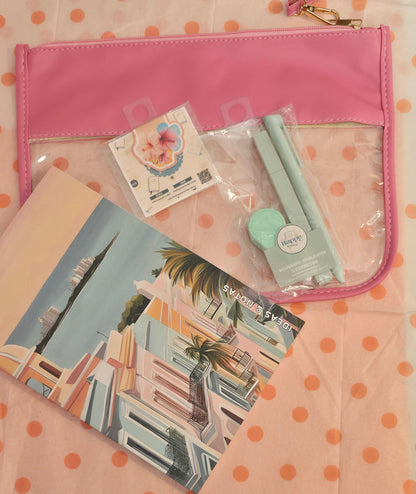 Collection of stationery items including a pink notebook, postcards, and a small bag on a polka dot surface.